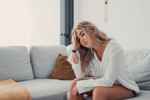 Femme assise sur un canapé, ressentant fatigue et tensions liées aux douleurs chroniques