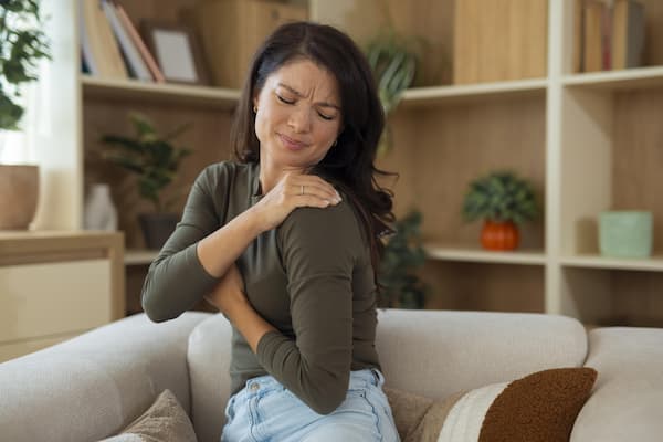 Femme ressentant une douleur persistante à l’épaule dans un intérieur calme